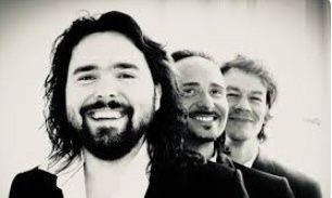 Ein Schwarz-Weiß-Foto von vier Männern mit Bärten und langen Haaren, die lächelnd für die Kamera posieren.