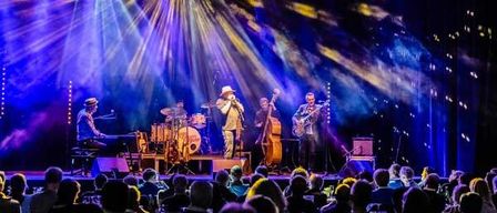 Eine Band spielt auf der Bühne unter leuchtenden Lichtern vor einem großen Publikum.