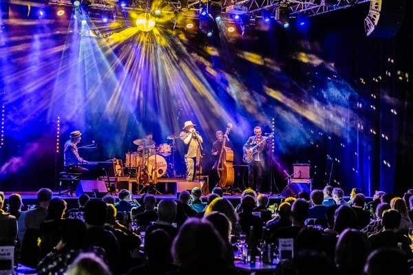 Eine Band spielt auf der Bühne unter leuchtenden Lichtern vor einem großen Publikum.