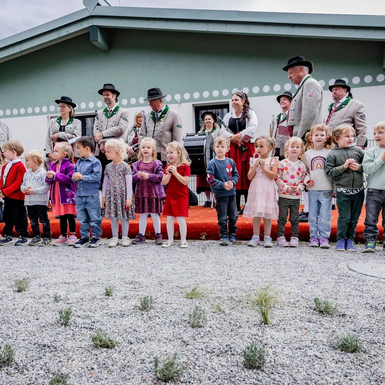 Eine Gruppe von Kindern und Erwachsenen steht vor einem Gebäude. Die Kinder tragen Kleider und die Erwachsenen tragen Hüte.