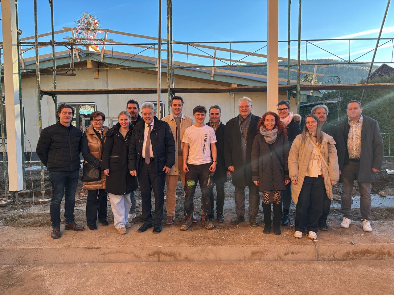 Eine Gruppe von Menschen in Winterkleidung posiert für ein Foto vor einem im Bau befindlichen Gebäude. Das Wetter ist sonnig.