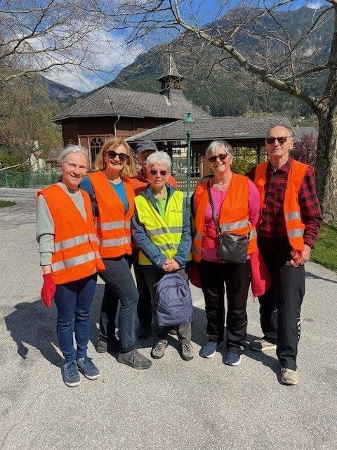 Five individuals in reflective vests, including three women and two men, pose for a photo on a sunny day in front of a building.