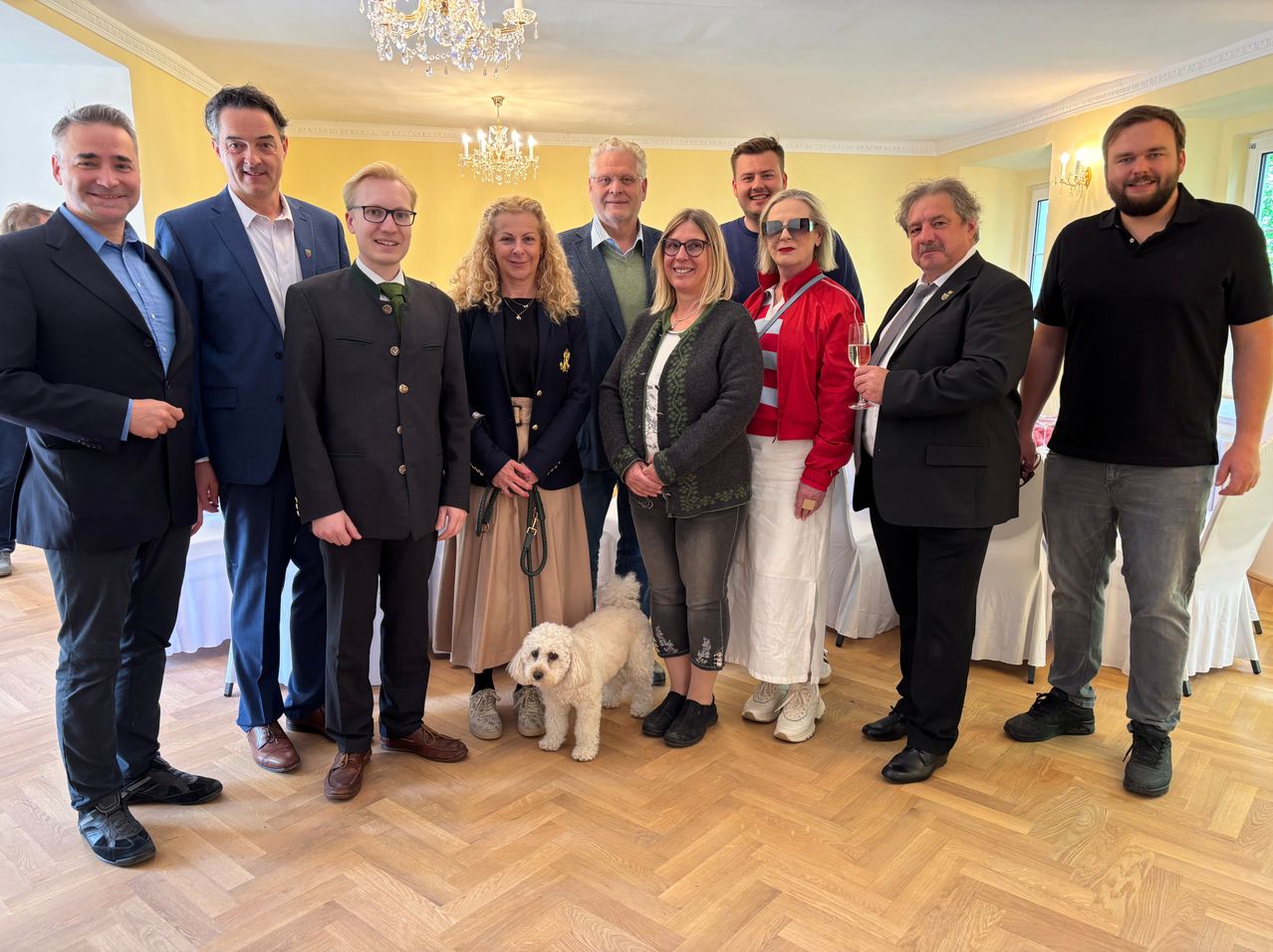 Eine Gruppe formell gekleideter Personen posiert mit einem Hund für ein Foto in einem dekorierten Raum.