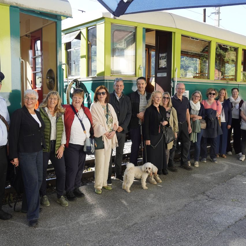 Eine Gruppe von Menschen, einschließlich eines Mannes in Uniform, steht vor einem Zug.