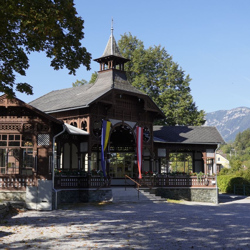 Ein hölzernes Pavillon mit einem Turm und Flaggen vor einem Gebirgszug.