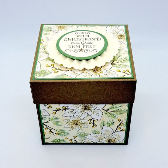 Eine dekorative Box mit Blumendesign, mit einem grünen Kreis, auf dem 'Vom Christkind Zum Fest' steht. Die Box ist braun und hat ein weißes Blumenmuster an den Seiten.