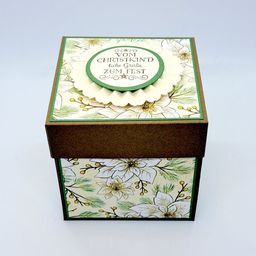 Eine dekorative Box mit Blumendesign, mit einem grünen Kreis, auf dem 'Vom Christkind Zum Fest' steht. Die Box ist braun und hat ein weißes Blumenmuster an den Seiten.