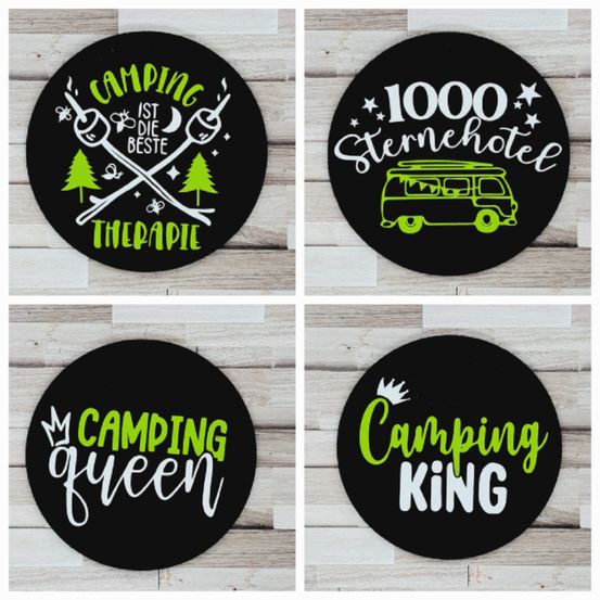 Vier schwarze runde Aufkleber auf einem hölzernen Hintergrund. Der obere linke lautet 'Camping ist die beste Therapie' mit Camping-Elementen. Der obere rechte sagt '1000 Sternehotel' mit einem Van-Motiv. Der untere linke sagt 'Camping queen' mit einer Krone. Der untere rechte sagt 'Camping King' mit einer Krone.