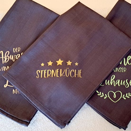Drei gefaltete braune Servietten mit goldenem Text 'STERNEKUCH' und 'DER ABW' darauf, mit Herz- und Blattdesign auf der rechten Seite.