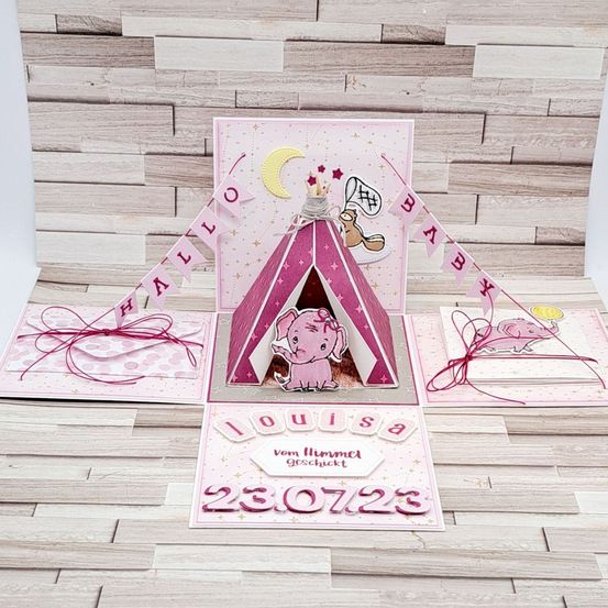 Eine rosafarbene Babyparty-Pop-up-Karte mit einem Zelt, einem Elefanten und einem Banner, das 'Hallo Baby' sagt. Die Karte ist mit rosa Bändern und Sternen verziert.