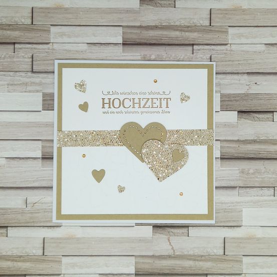 Eine Hochzeitskarte mit goldenen Glitzerherzen und einer Botschaft auf Deutsch. Die Karte hat einen hölzernen Hintergrund.
