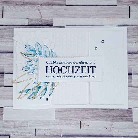 Eine handgefertigte Karte mit blauem Blumendesign und goldenen Akzenten, die einen deutschen Text enthält, der eine schöne Hochzeit und ein schönes zukünftiges Leben wünscht. Die Karte liegt auf einer Holzoberfläche.