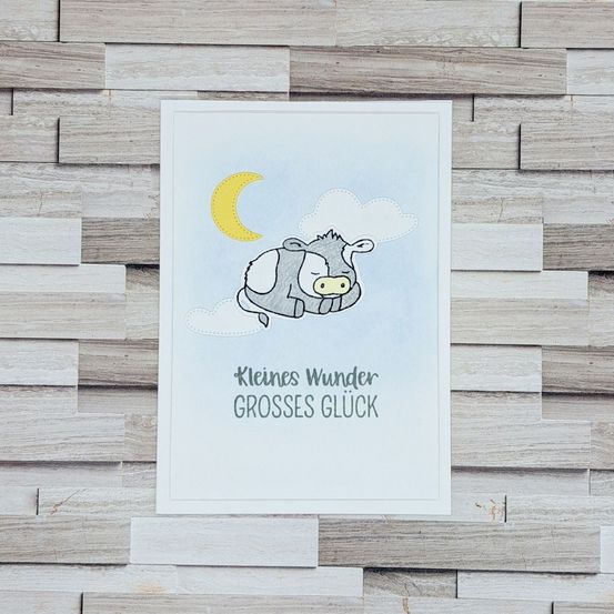 Eine Karte mit einer schlafenden Kuh unter einem Halbmond und Wolken, mit dem Text 'Kleines Wunder Grosses Gluck'.