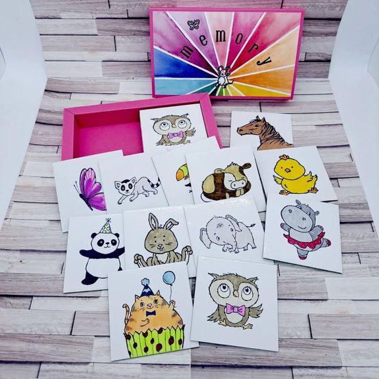 Eine Reihe von tierthematischen Karten mit verschiedenen Illustrationen, darunter eine Eule, ein Pferd und ein Panda, auf einer Holzoberfläche angeordnet, mit einer farbenfrohen Box im Hintergrund, die mit 'Memory' beschriftet ist.