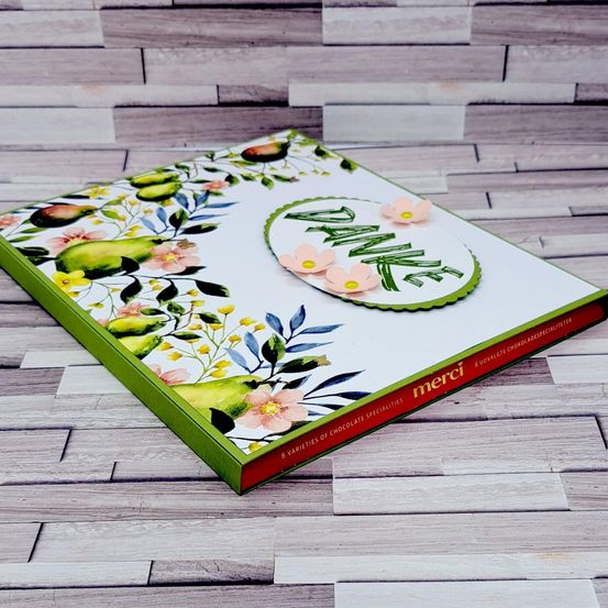 Eine grüne Box mit einem Blumendesign auf dem Cover, mit Birnen und Blumen, mit dem Wort Danke in Grün. Die Box liegt auf einer hölzernen Oberfläche.