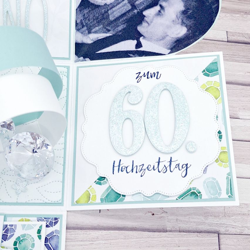 Eine handgefertigte Karte mit der Nummer 60 und den Worten 'Hochzeitstag' in silbernem Glitzer auf weißem Hintergrund, mit einer Fotocollage im Hintergrund.