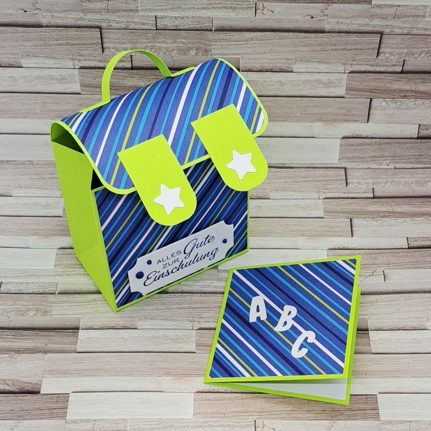 Eine grün-blau gestreifte Tasche mit einem Griff und zwei grünen Sternen auf der Vorderseite, neben einer gefalteten Karte mit den Buchstaben ABC.