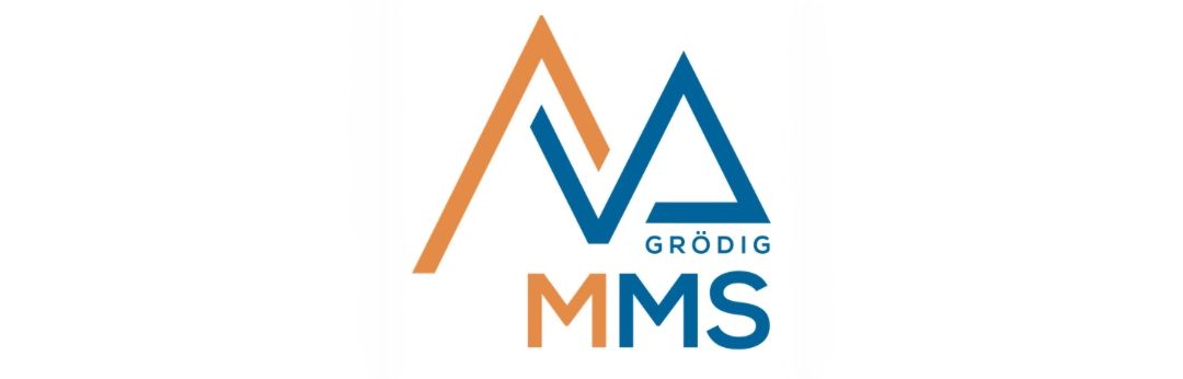 Das Bild zeigt das Logo für Grödig MMS. Es hat ein stilisiertes 'V' mit dem Wort 'Grödig' darunter und 'MMS' in großen blauen Buchstaben. Das Logo ist auf einem weißen Hintergrund gesetzt.