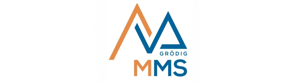 Das Bild zeigt das Logo für Grödig MMS. Es hat ein stilisiertes 'V' mit dem Wort 'Grödig' darunter und 'MMS' in großen blauen Buchstaben. Das Logo ist auf einem weißen Hintergrund gesetzt.