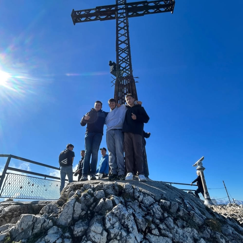 Eine Gruppe von Menschen steht auf einem felsigen Hügel mit einem großen Kreuz im Hintergrund.
