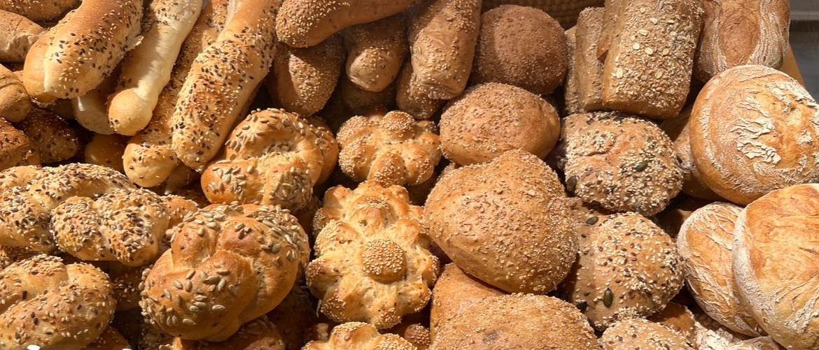 Ein Korb voller verschiedener Brote mit Sesam und Samen, einschließlich Baguettes, runden und langen Laibbroten.