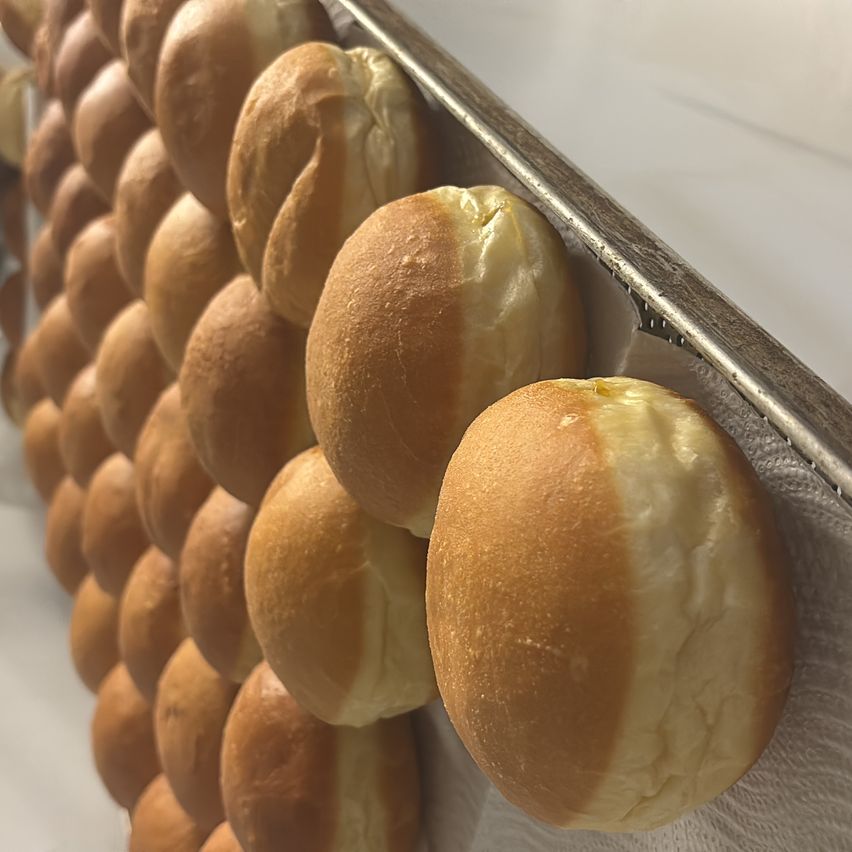 A close-up view of numerous golden-brown buns arranged in rows, with some visible folds and a light-colored lining.