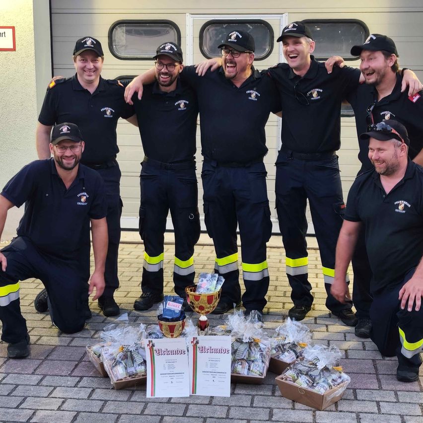 A group of firefighters in uniform are posing for a photo with a trophy and various gift boxes in front of them.