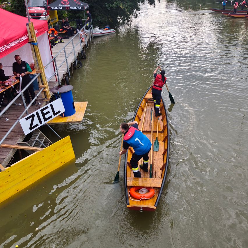 Ein Boot mit zwei paddelnden Personen auf einem Fluss, in der Nähe eines Stegs mit einem Schild, das 'Ziel' bedeutet.