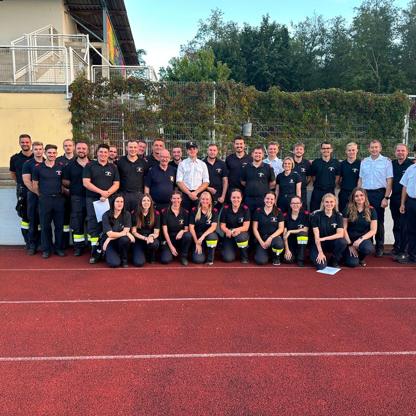 Eine Gruppe Feuerwehrleute in Uniform posiert für ein Foto auf einer roten Laufbahn.