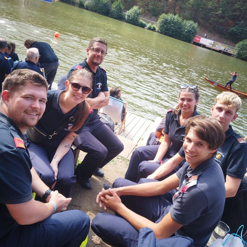 Eine Gruppe von Menschen in Uniform sitzt auf einem Steg am Fluss und posiert für ein Foto.