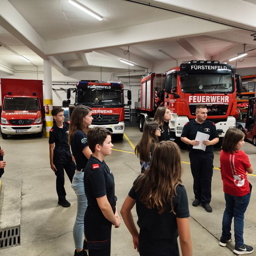 Eine Gruppe von Kindern und ein Mann in Feuerwehruniform stehen in einer Garage mit Feuerwehrautos.