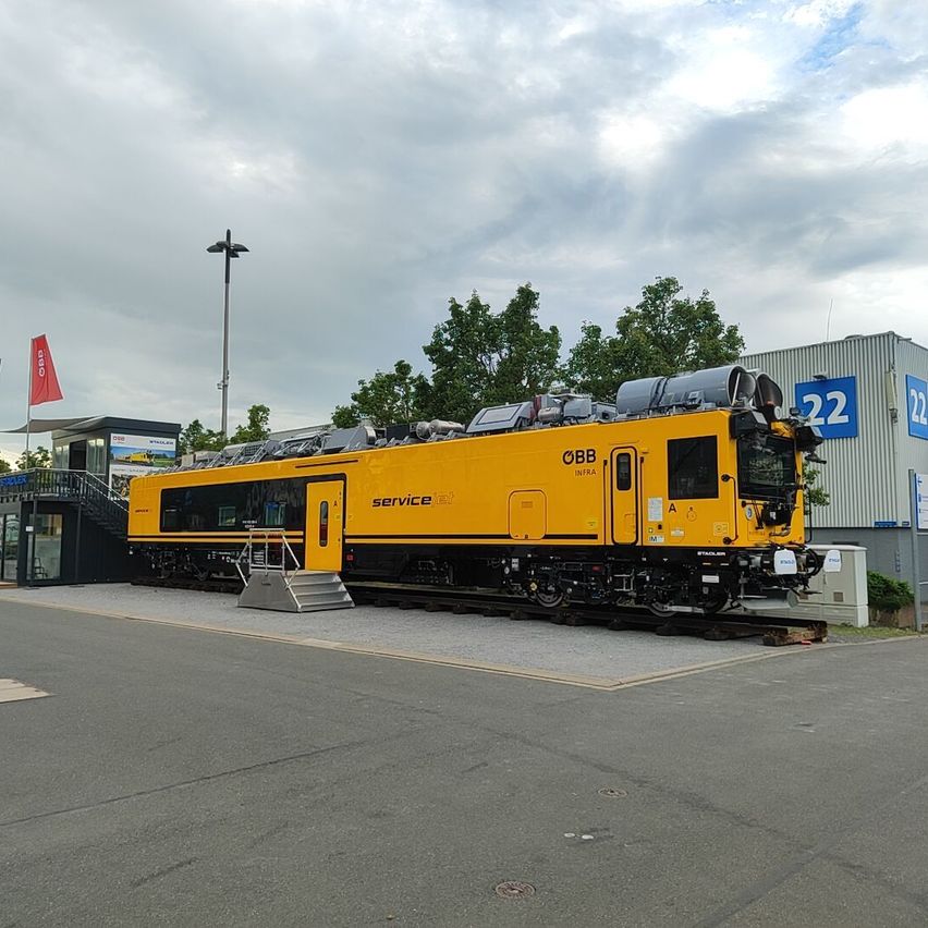 A yellow train with the word service on it is parked on the tracks. A building with a red flag and a sign with the number 22 is behind it.