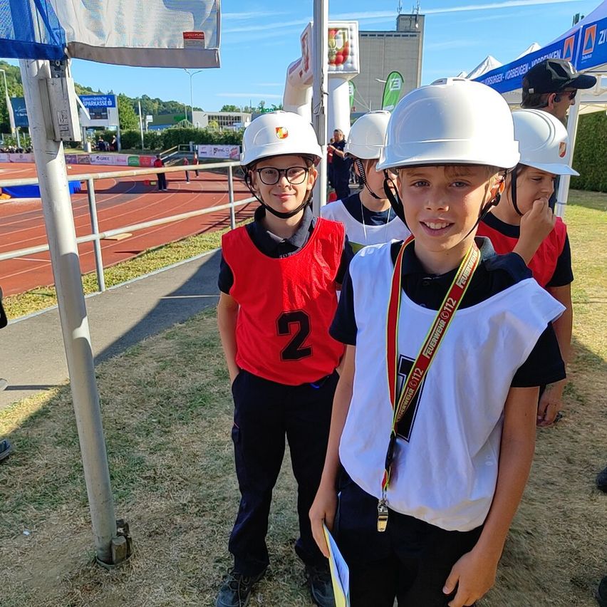 Zwei junge Jungen in roten und weißen Westen und weißen Helmen stehen nebeneinander bei einer Sportveranstaltung.