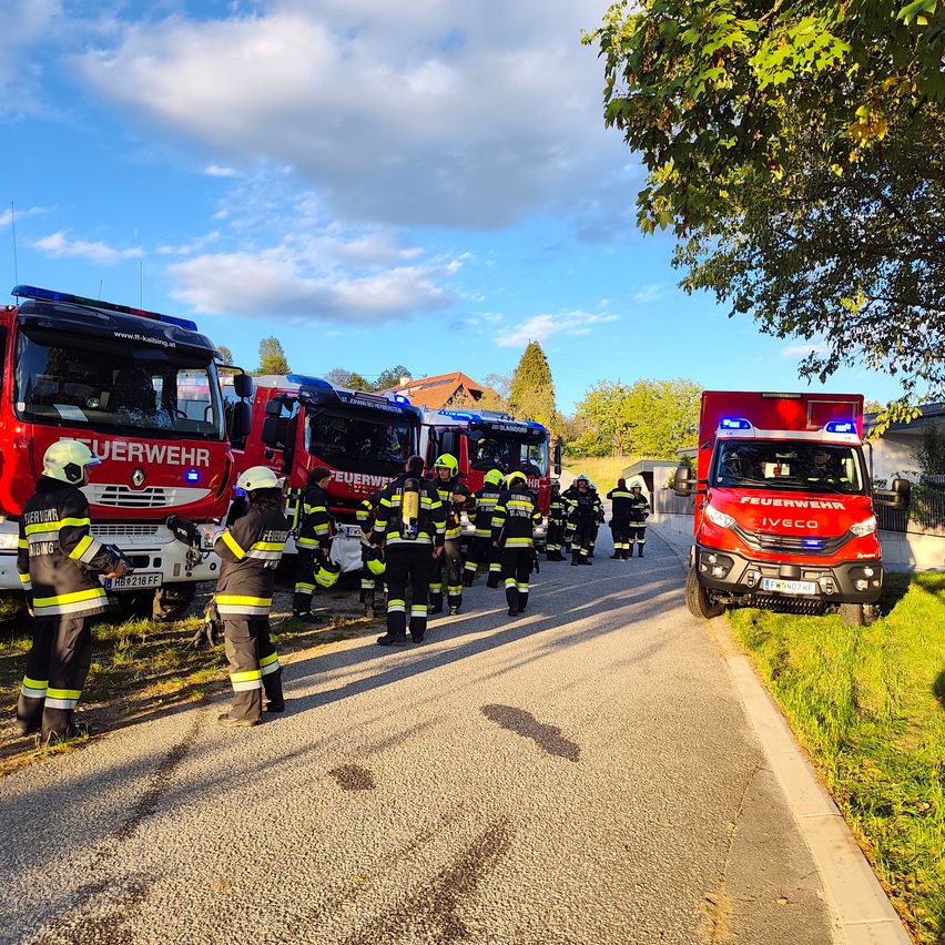 Eine Gruppe von Feuerwehrleuten in Uniform steht vor einer Reihe von Feuerwehrwagen auf einer Straße.