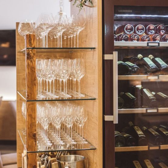 Ein hölzerner Weinregal mit mehreren Glasablagen hält Weingläser. Daneben steht ein Weinkühler gefüllt mit verschiedenen Weinflaschen.