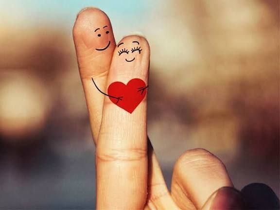 Eine Hand mit Fingern, die in einem lächelnden Gesicht und einem Herzen gezeichnet sind, wird in Nahaufnahme gezeigt. Das Herz ist rot mit einem glücklichen Ausdruck.