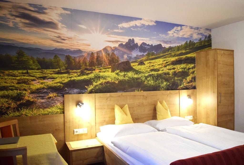 Ein Hotelzimmer mit einem Bett, das zwei weiße Kissen und zwei gelbe Kissen aufweist. Der Raum hat eine große Wandmalerei einer Berglandschaft.