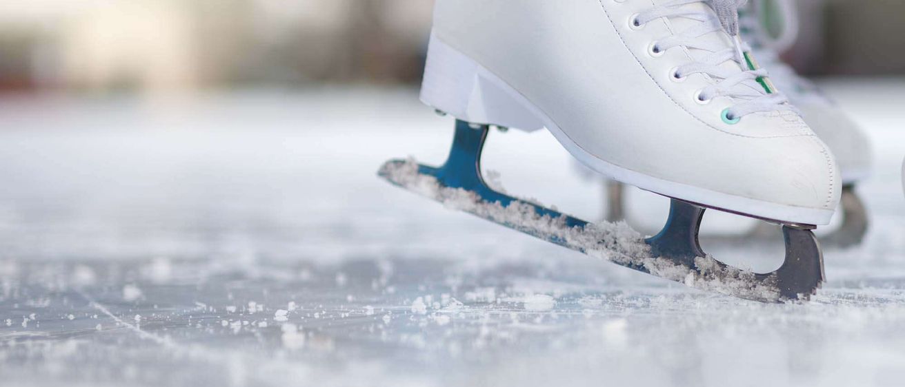 Eine Nahaufnahme eines weißen Eislaufschuhs mit blauen Klingen, bedeckt mit Schnee, auf einer Eisbahn.