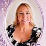 Eine Frau mit blondem Haar, die ein schwarz-weißes Oberteil und rosa Ohrringe trägt, lächelt vor einem lila Herzen und Blättern.