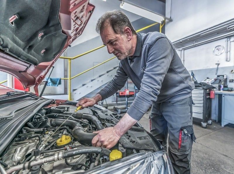 Ein Mann in einer Garage arbeitet mit einem gelben Werkzeug an einem Automotor.