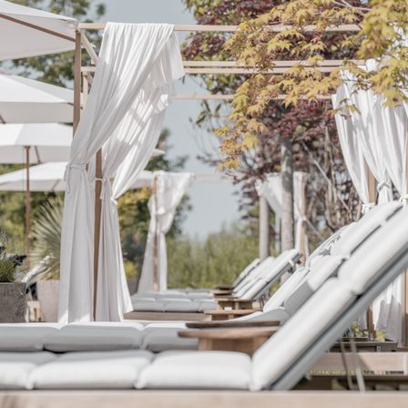 Ein Blick auf einen Außenbereich mit weißen Liegestühlen und weißen Vorhängen.