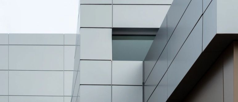 Nahaufnahme eines modernen Gebäudes mit weißen und grauen Paneelen, einem Fenster und einem leicht gebogenen Dach unter einem klaren Himmel.