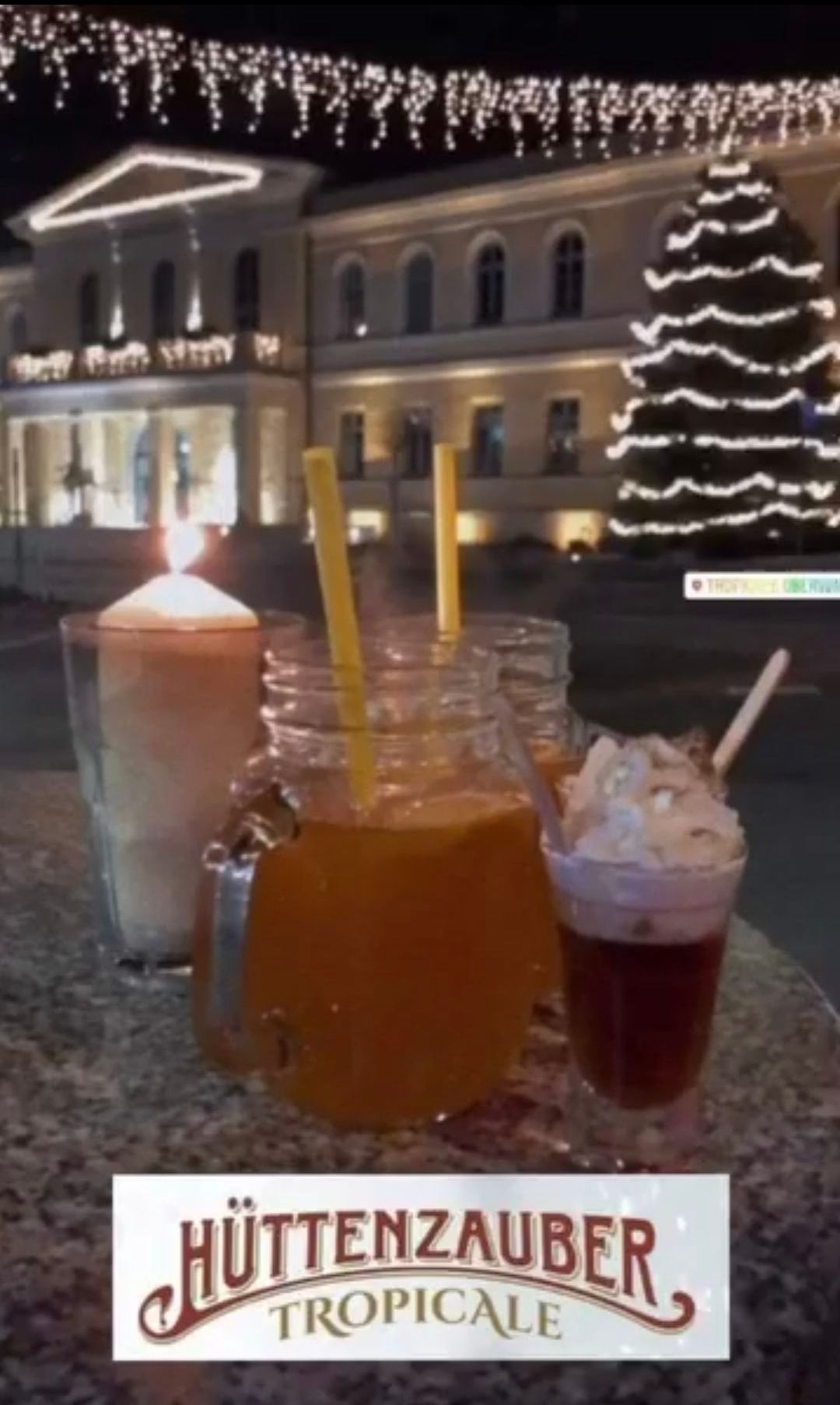Ein Tisch mit mehreren Getränken, darunter eine Kerze und ein Weihnachtsbaum im Hintergrund.