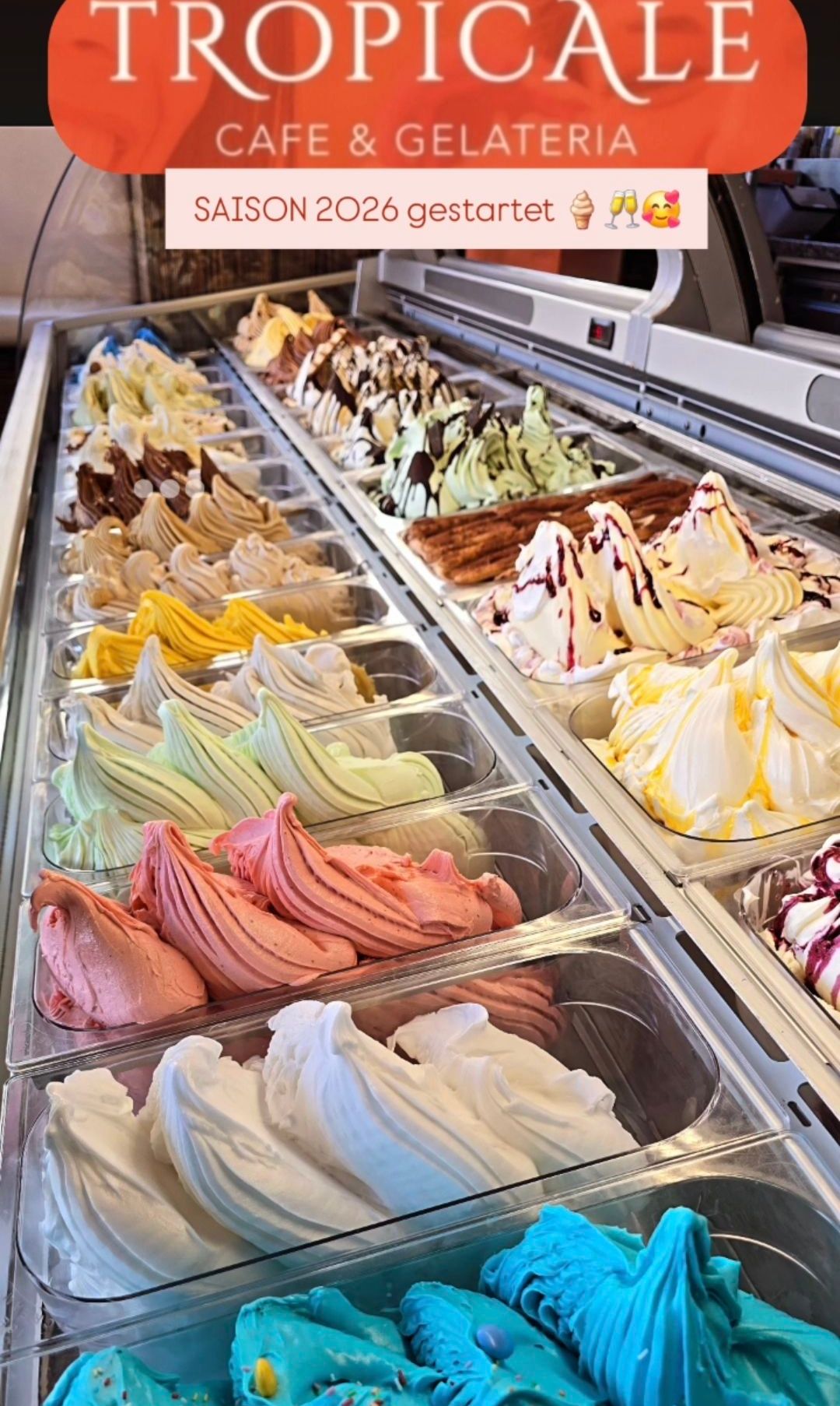 Eine Vielzahl von Eiscremesorten wird in einem Geschäft ausgestellt, darunter Schokolade, Vanille, Erdbeere und mehr. Das Eis ist in verschiedenen Formen und Farben und einige haben Toppings. Das Bild ist von der Vorderseite der Ausstellung aufgenommen.