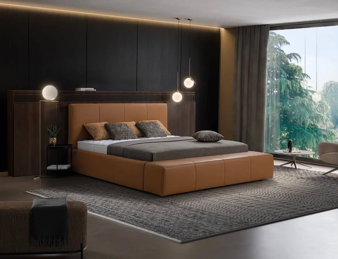 Ein modernes Schlafzimmer mit einem großen braunen Lederbett, geschmückt mit mehreren Kissen, steht vor einem dunklen Hintergrund. Zwei Lampen hängen von der Decke, und natürliches Licht flutet durch große Fenster in den Raum.