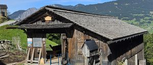 Ein altes Holzgebäude mit einem Schieferdach, in einem Gebirgsgebiet gelegen. Ein Schild über dem Eingang trägt die Aufschrift '1790'. Draußen stehen ein Besen und ein Eimer.