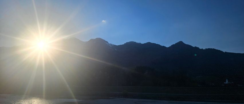 Die Sonne geht über einer Berglandschaft auf und taucht das Wasser darunter in ein warmes Licht.