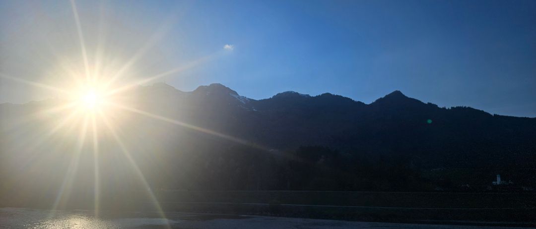 Die Sonne geht über einer Berglandschaft auf und taucht das Wasser darunter in ein warmes Licht.