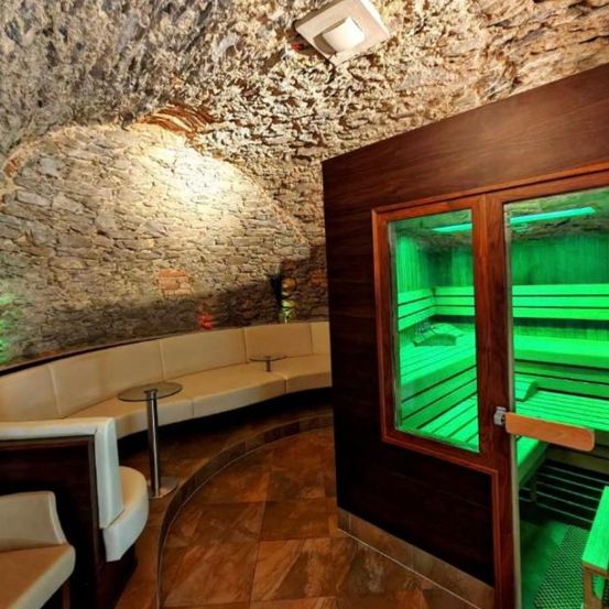 Ein gemütlicher Saunaraum mit einer Steinwand, einer Bank und einem Tisch, beleuchtet von grünen Lichtern.