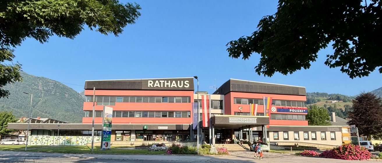 Ein rotes Rathaus-Gebäude mit einer Polizeistation auf der rechten Seite, zwei Personen gehen davor.